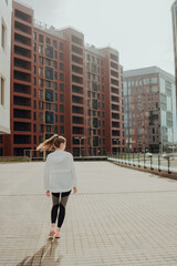 Naklejka premium A young blonde sports girl in a black suit runs along modern houses