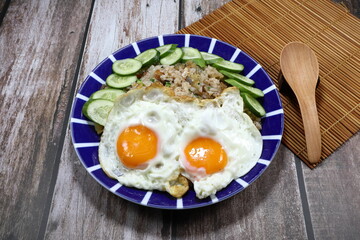 Traditional fried rice topping with double fried egg and sliced fresh cucumber on the plate. Famous special street food in Asia restaurant. 