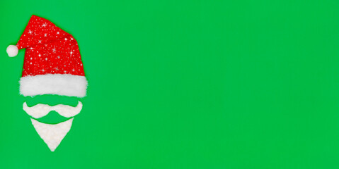 Christmas background. Santa Claus red hat, white mustache and beard on a green backdrop with copy space. Baner. New Year. Flat lay, top view