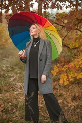 Blonde nice woman at autumn coat and colorful umbrella at park. Pretty plus size European lady