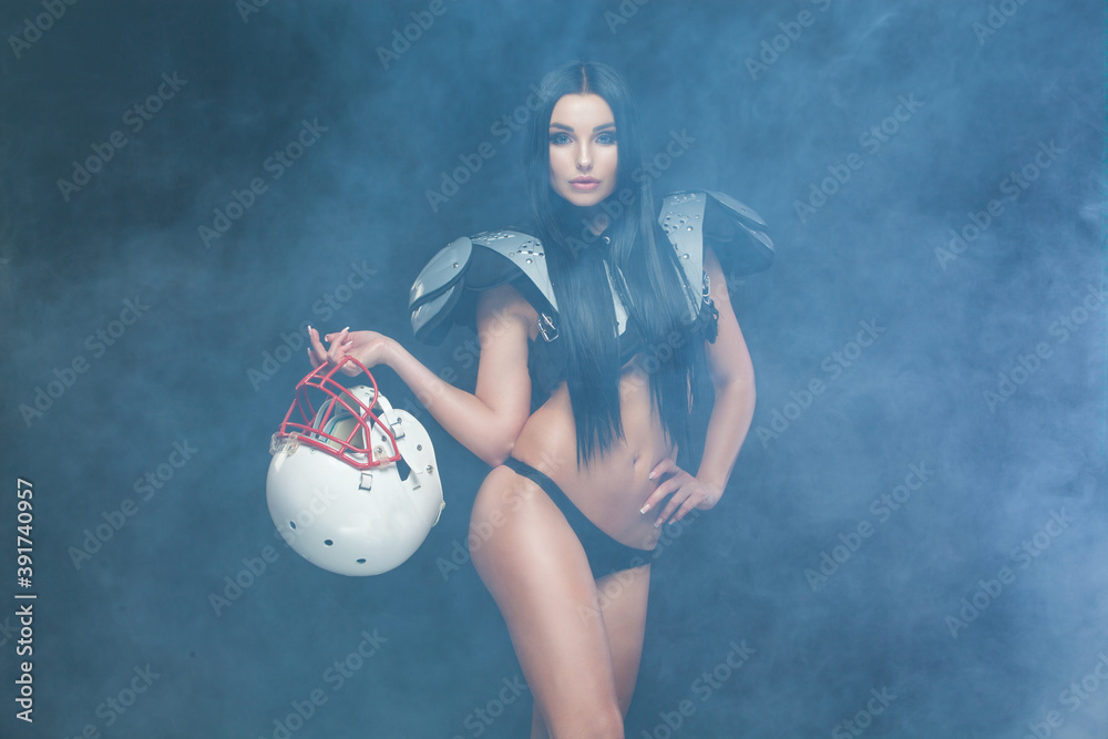 Sticker American football. Front view of young sporty brunette wearing sexy uniform of rugby football player posing with helmet in smoke isolated on black background