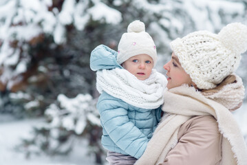 Young mother of the family holding a little daughter in her arms, walking through the winter forest
