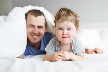 family, love, happiness and fatherhood concept - happy father and cute little girl daughter having fun in bed