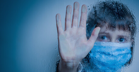 Fear of young girl due to coronavirus pandemic. Close up female child wearing medical face mask for protect pm2.5 and showing stop gesture from behind glass. Copy space for design.