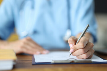 Doctor holding in hand silver pen on documents at table in office close-up. Documentation in medicine concept