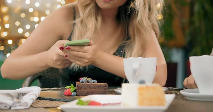 pretty blonde girlfriend taking picture of delicious chocolate cake in restaurant against fairy lights slow motion