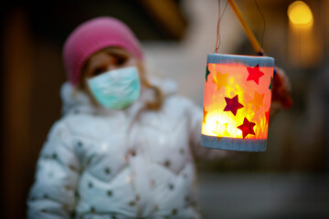 Toddler girl holding selfmade lantern for St. Martin procession. Child wear medical mask. children...