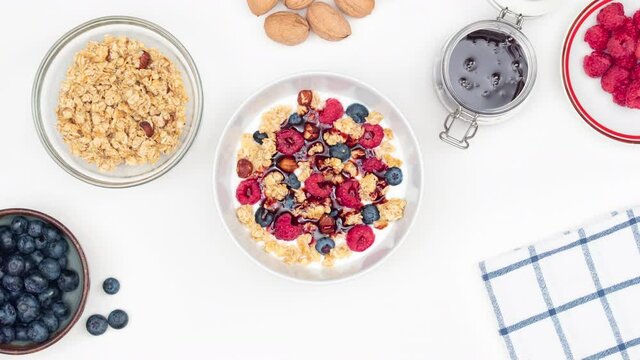 Top view on blueberries and raspberries jumping to a bowl with yoghurt. Healthy breakfast with forest fruits and toasted muesli. Stop motion animation.