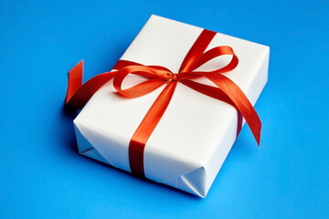 White gift box tied with red ribbon on blue background
