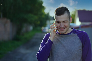 Man speaking on smartphone in suburb. Adult male in casual clothes answering phone call on blurred background of suburban street