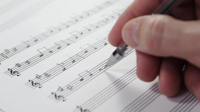 The hand of an unknown musician writes the notes of a composition on a pentagram.
