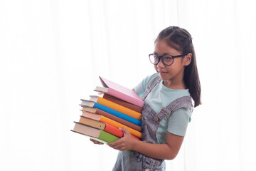 Adorable Asian smart girl in casual jean hold stack of books, adorable intelligent school girl primary looking her many book with happy, girl study at home social distance back to school concept
