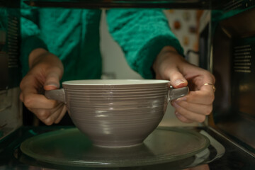 Women's hands take a plate out of the microwave, photo from inside