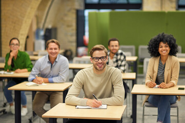 Business lecture. Group of happy multiracial people sitting in the modern office and listening to coach or speaker during seminar, selective focus on cheerful caucasian man