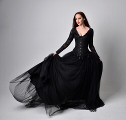 full length portrait of  woman wearing black gothic dress,  Standing pose  against a studio...