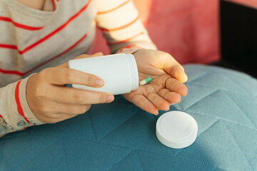 Patient taking medicine pill from white bottle at hone.