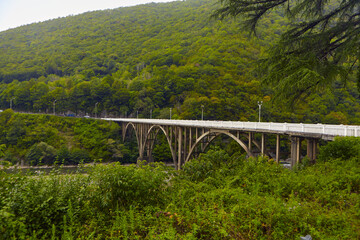 Obraz premium The mountain river along the Road, of a scenic highway by the beautiful Landscape covered in clouds and fog, bridge and viaduct, The mountain river along the road,