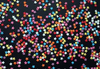 Fototapeta na wymiar multicolored confetti stars on dark background. Festive background. 