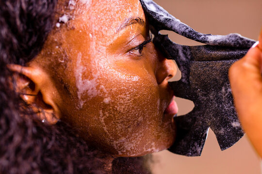 Young woman with bubble sheet mask on her face on brown background