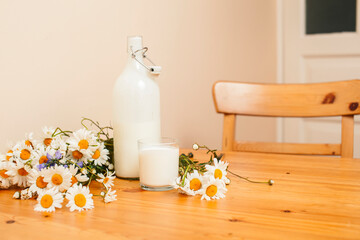 Simply stylish wooden kitchen with bottle of milk and glass on table, summer flowers camomile, healthy foog moring concept