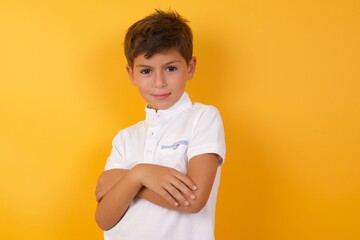 Honest Young handsome Caucasian little boy standing against yellow wall keeps hands on chest,...