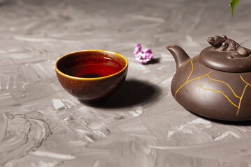 Chinese tea. Tea bowl and teapot on a dark background. Lilac flowers in a vase