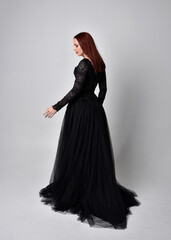 full length portrait of  woman wearing black gothic dress,  Standing pose  against a studio background.