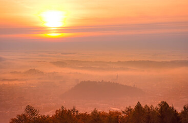 Amazing foggy sunrise over the city of Graz with Schlossberg hill and Church of the Sacred Heart of Jesus tower, in Styria region, Austria. Panoramic view from Plabutsch mountain on autumn morning.