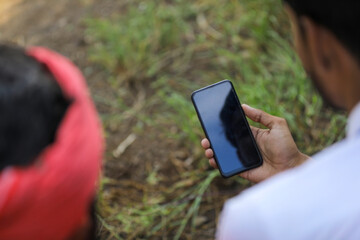 Young indian agronomist or banker showing some information to farmer in smart phone