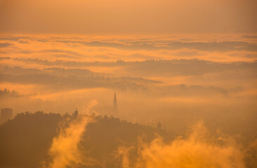 Amazing foggy sunrise over the city of Graz with Schlossberg hill and Church of the Sacred Heart of Jesus tower, in Styria region, Austria. Panoramic view from Plabutsch mountain on autumn morning.