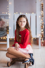 A cute teenage girl sits on a wooden sled in a Christmas interior with a Christmas tree and bokeh. Christmas and New Year concept