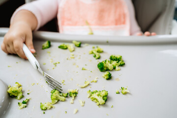 Little caucasian girl picking vegetables from a feeder in kitchen with fork, full vegan or...