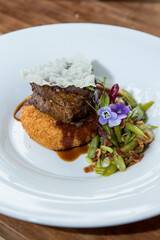 Tasty portion of meat cooked in its sauce on a bed of gratin mashed potatoes, accompanied by vegetables.