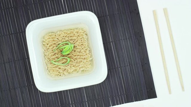 Instant noodles growing in ceramic bowl on bamboo black mat and white background with chopsticks. Top view time lapse and stop motion animation. Fast food concept.