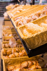fresh golden breads with melted cheese wrapped in plastic wrap in wicker basket in bread department of supermarket