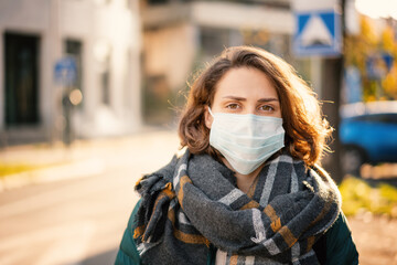 Portrait of a beautiful young European woman in a protective mask on a city street. Antiviral...