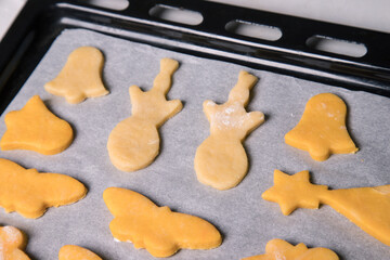 Homemade cookies in the form of butterflies, bells and snowmen before baking on a baking sheet, close-up. Horizontal orientation