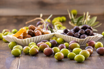 Green, black olives inside and outside in white bowl on wooden background.