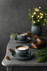 Obraz na płótnie Canvas A photo of cappuccino with chocolate donuts and christmas decoration. Grey cups on the grey table and a grey wall. Place for text