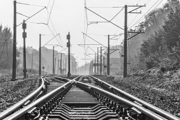Two railway tracks with electric power poles and cables near a small township's train station....