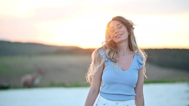 Happy blonde woman dancing at sunset in Moldova, shaking head with long hair