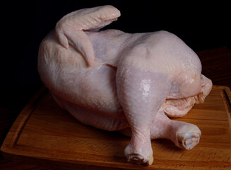 Chicken broiler in an interesting pose lies on a wooden cutting board.
