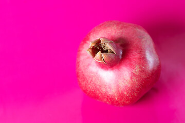 one whole pomegranate fruit with leaves on a bright pink background