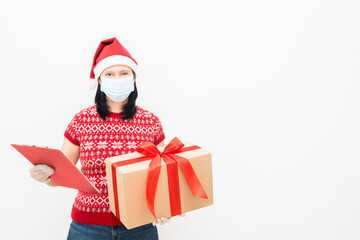 Fototapeta na wymiar Woman courier in a santa hat and a medical mask holding a gift on a light background