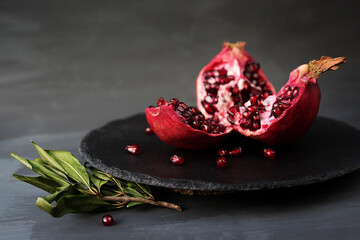 broken into pieces pomegranate fruit with leaves on a black round stand of slate black background