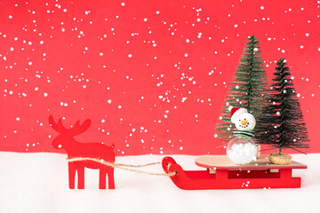 Toy reindeer and sleigh delivering christmas trees on red background