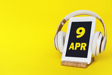 April 9th. Day 9 of month, Calendar date. Stylish headphones and modern tablet on yellow...
