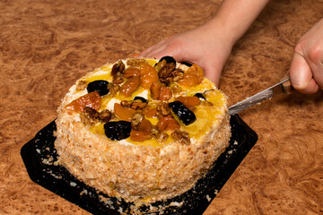 A festive cake on the table cuts a woman's hand with a knife. The concept of celebrating the holiday