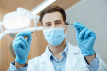 Millennial friendly stomatologist in white coat, protective mask and rubber gloves working with professional equipment