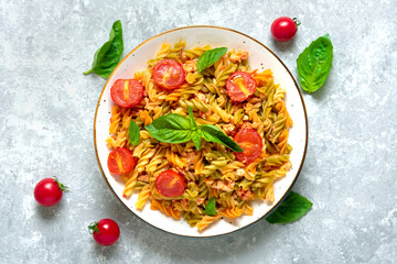 Fusilli - classic italian pasta from durum wheat with chicken meat, tomatoes cherry, basil in tomato sauce in white bowl on gray concrete table Mediterranean cuisine Top view Flat lay